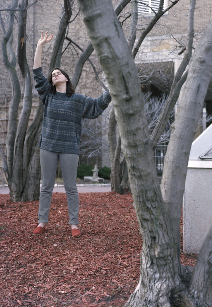 AJ stands in a tree grove, hands raised