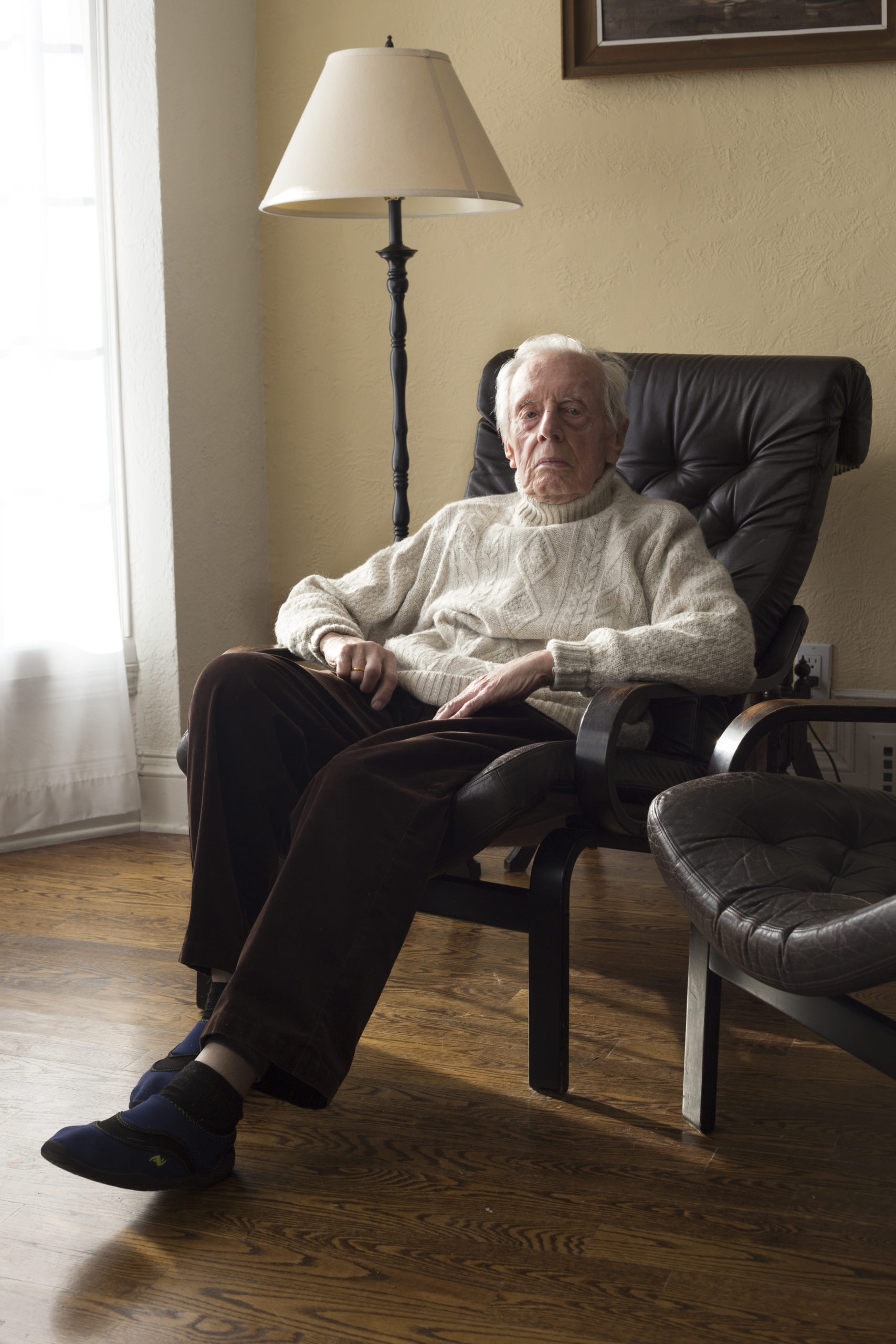 An older gentleman sits in a leather armchair and looks directly into the camera