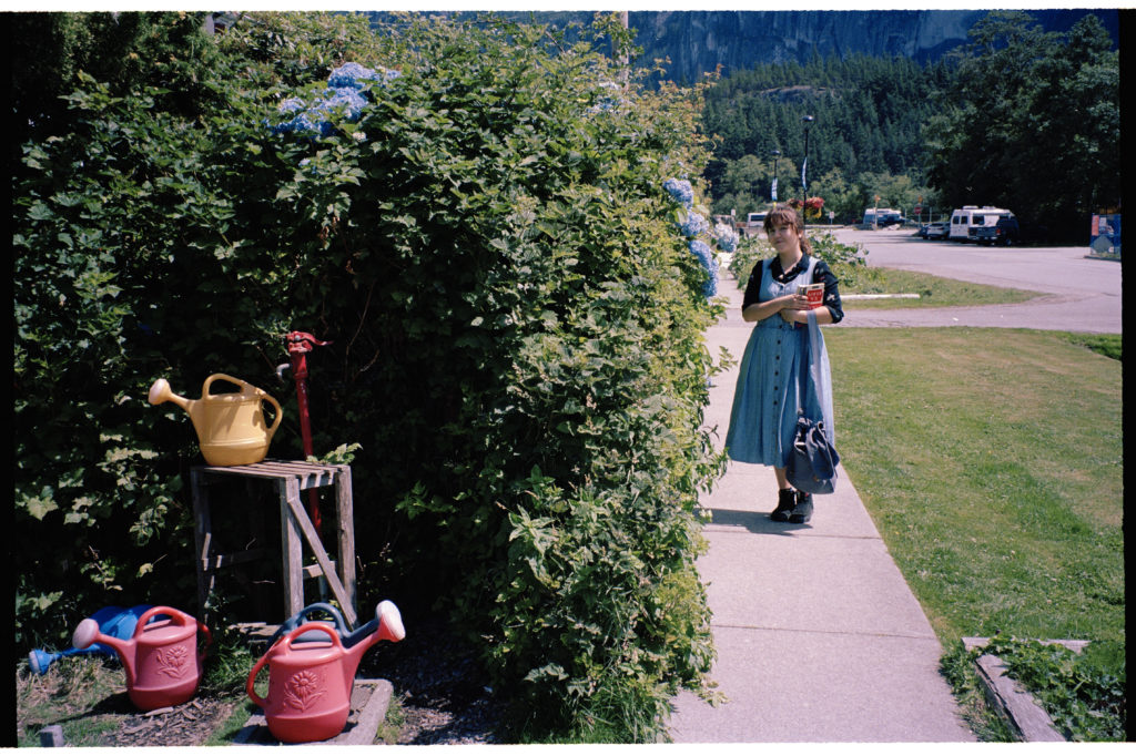 Self portrait with watering cans and a blue Hydrangea bush