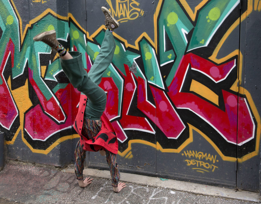 Aisha does a handstand in front o a piece of graffiti that matches her clothes