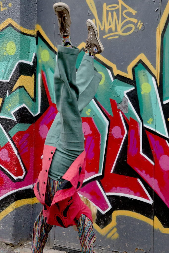 Aisha does a handstand in front of a piece of graffiti that matches her clothes